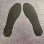 A close-up image of carbon fibre insoles next to a pair of sports shoes.